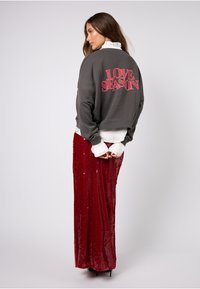 Šedá mikina s červeným potiskem "LOVE SEASON" na zádech, doplněná dlouhou červenou flitrovou sukní s lesklou texturou a přiléhavým střihem.