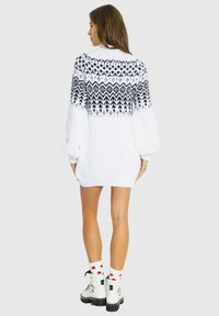Biała, oversize sukienka sweterkowa z czarnym geometrycznym wzorem na ramionach. Długie rękawy i teksturowane, dzianinowe wykończenie.