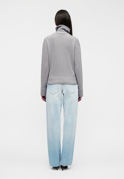 Γκρι φλις πουλόβερ με ψηλό γιακά, άνετη εφαρμογή και ριμπ τελείωμα, σε συνδυασμό με ανοιχτό μπλε τζιν παντελόνι με φαρδιά πόδια.