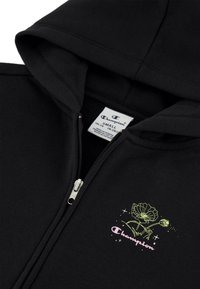 Sudadera con cremallera en color negro, hecha de una mezcla de algodón, que presenta una cremallera frontal y un gráfico floral en verde y rosa con el logo "Champion".