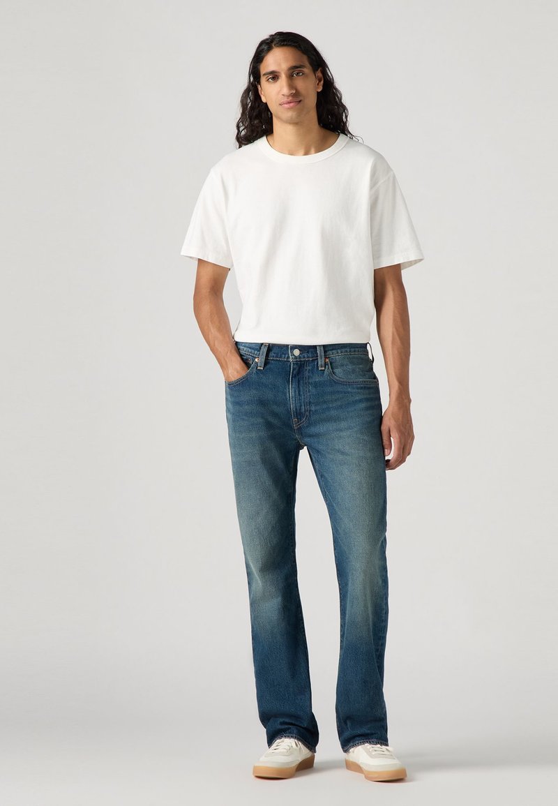 Vit t-shirt med kort ärm, parat med blå raka jeans med en blekt tvätt, och vita sneakers med beige sulor.