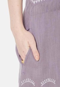 Lavanda pletena haljina s teksturiranim uzorkom, koja sadrži bočnu džep i vezenje na rubu. Ruka počiva u džepu.