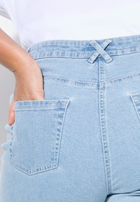 Světle modré džíny s vysokým pasem, viditelným švem, dvěma zadními kapsami a křížovým designem v pase.