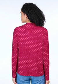 Langarmshirt in Burgunderrot mit rosa Punkten, mit rundem Halsausschnitt und abgerundetem Saum, aus einem weichen, elastischen Stoff.