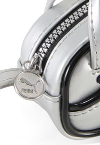 Borsa accessorio argento con finitura testurizzata, zip nera e charm del logo Puma metallico. Forma curva con elementi di design eleganti.