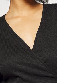 Svart omslagstopp med djup V-ringning, ribbad struktur och korta ärmar. Materialet verkar lätt och mjukt.