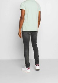 Camiseta de manga corta verde menta, corte relajado, combinada con jeans ajustados gris oscuro y zapatillas blancas con acentos rojos. Diseño simple y casual.