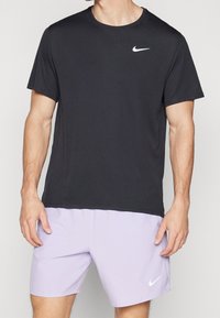 Camiseta negra de Nike de manga corta con cuello redondo y logo blanco en el pecho, combinada con pantalones cortos lilas claros que tienen un logo blanco.