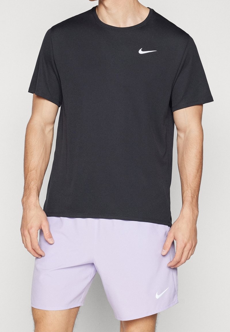 Camiseta negra de Nike de manga corta con cuello redondo y logo blanco en el pecho, combinada con pantalones cortos lilas claros que tienen un logo blanco.
