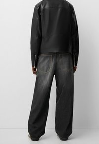 Giacca di pelle nera con un design aderente, abbinata a jeans in denim scuro a gamba larga con tasche posteriori visibili e cuciture a contrasto.