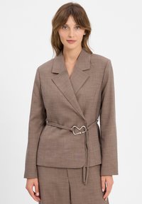 Blazer marron texturé avec un col cranté, taille cintrée à l'aide d'une ceinture en métal argenté, et design ajusté.