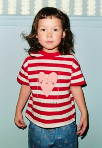 Red and white striped T-shirt featuring a pink heart graphic with a smiling face, complemented by blue denim pants with cherry patterns.