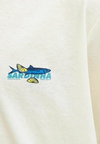Illustratie van een blauwe sardine met schijfjes citroen en blauwe tekst "SARDINHA" op een beige stoffen achtergrond.