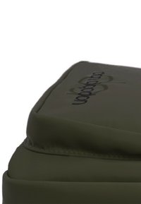 Mochila verde oliva con una superficie texturizada, que presenta una parte superior acolchada y un logotipo bordado en hilo oscuro. Diseño minimalista, forma funcional.