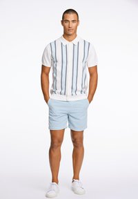 Kurzarm-weißer Poloshirt mit marineblauen vertikalen Streifen, kombiniert mit hellblauen Shorts. Weiße Sneakers runden das Outfit ab.