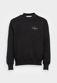 Sudadera negra de cuello redondo fabricada con una mezcla de algodón. Presenta puños y dobladillo acanalados, con un pequeño logo blanco de "Calvin Klein Jeans" en el pecho.
