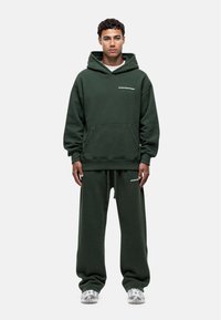 Felpa con cappuccio verde in cotone e pantaloni della tuta coordinati, dal taglio rilassato. Presenta una tasca frontale e un semplice logo testuale sul petto.