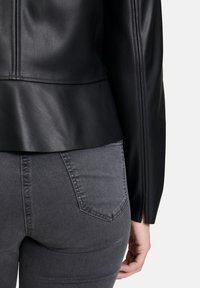 Svart läderjacka med peplumdesign, med mjuk textur och synliga sömmar, i kombination med grå tajta jeans med bakfickor.