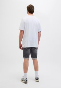 Tricou alb din bumbac, pantaloni scurți din denim gri cu tivuri răsfrânte, șosete albe și adidași gri. Vedere din spate, pe un fundal alb simplu.