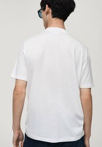 Bílý bavlněný tričko s krátkými rukávy, volný střih a kulatým výstřihem. Bezešvý design bez výrazných vzorů nebo akcentů.