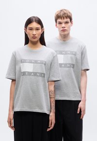 Γκρι βαμβακερά t-shirts με κουτί σχήματος, με εκτυπωμένο κεντρικά λογότυπο που γράφει "TOMMY JEANS" σε αντίθετα χρώματα στο μπροστινό μέρος.