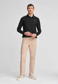 Zwart poloshirt met lange mouwen, kraag en een drieknopenlijst, gecombineerd met lichtbeige broek en beige sneakers.