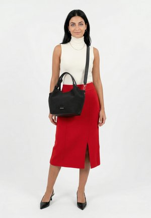 Frau trägt ärmellosen weißen Rollkragenpullover, roten Midirock mit Frontschlitz, schwarze High Heels, trägt schwarze Handtasche mit Schultergurt.