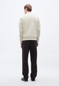 Φωτεινή μπεζ φούτερ με ελαφρώς υφή επιφάνεια, σε συνδυασμό με μαύρο, φαρδύ παντελόνι. Ορατές λεπτομέρειες με ριμπ μανσέτες και μέση.