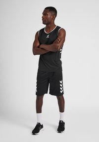 Black athletic tank top with white accents, paired with black shorts featuring white chevron patterns. Black sneakers and white socks complete the look.