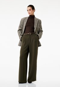 Gråternet blazer over en brun turtleneck, parret med høj talje olivenbukser. Detaljer inkluderer et brunt bælte og en flagrende silhuet.
