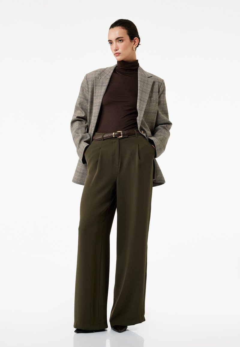 Gråternet blazer over en brun turtleneck, parret med høj talje olivenbukser. Detaljer inkluderer et brunt bælte og en flagrende silhuet.