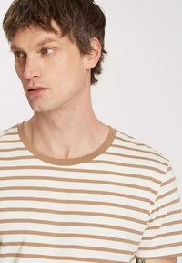 Pasiasta koszulka z okrągłym dekoltem, wykonana z miękkiego materiału. Pasy są beżowe i białe, z jednolitym beżowym wykończeniem przy kołnierzu.