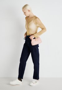 Sheer gold long-sleeve top paired with dark blue straight-leg jeans. Carrying a small pink quilted purse with a chain strap and white sneakers.