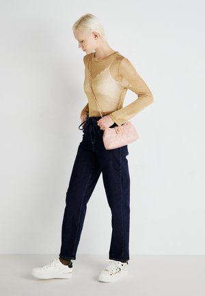 Przezroczysta złota bluzka z długim rękawem zestawiona z ciemnoniebieskimi spodniami o prostym kroju. Niesie małą różową pikowaną torebkę na łańcuszku oraz białe trampki.