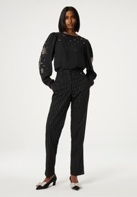 Zwarte blouse met opbollende mouwen versierd met zilveren sterrenborduursels, gecombineerd met zwarte pinstripe broeken en zwarte hakken met glinsterende accenten.