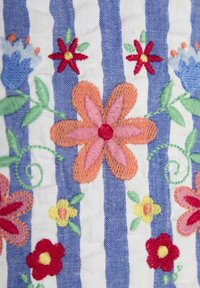 La tela bordada presenta flores multicolores en rosa, rojo, amarillo y azul sobre un fondo de rayas blancas y azules. Acabado texturizado.