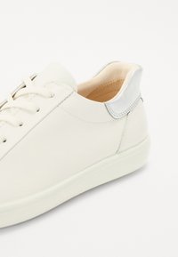 Sneaker bianca in pelle con una finitura liscia, punta arrotondata e lacci tono su tono. Presenta un interno morbido di colore chiaro e un accento metallico sul tallone.