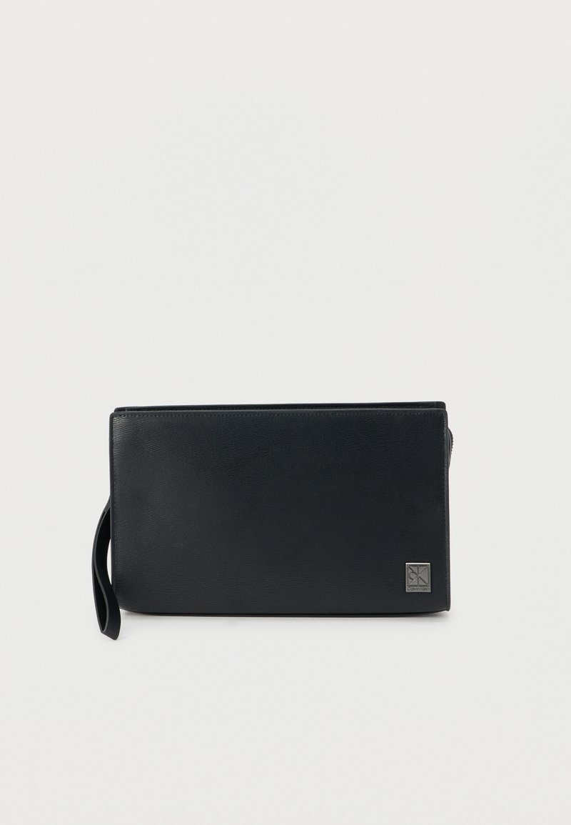 Μαύρο τσαντάκι από δέρμα με λεία υφή, ορθογώνιο σχήμα, κλείσιμο με φερμουάρ και λουράκι για τον καρπό. Διαθέτει ένα μικρό ανάγλυφο λογότυπο στο μπροστινό μέρος.