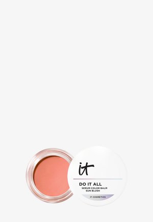 Pot transparent contenant un baume couleur sérum ton pêche avec un couvercle blanc, étiqueté "it DO IT ALL Serum Color Balm Sun Blush" sur un fond blanc.