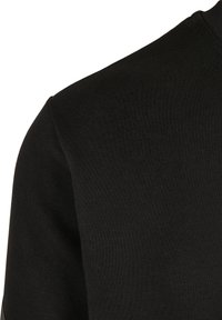 Gros plan d’un tissu noir montrant les détails des coutures d’épaule et de manche d’un vêtement uni à manches longues.