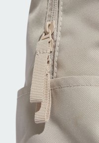 Tejido beige con una superfície texturizada, que presenta una cremallera y una correa con lazo. El tirador de la cremallera es de un color claro en contraste.