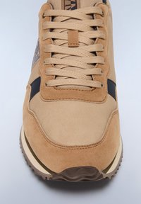 Sneaker sintetico marrone chiaro con finitura in suede, caratterizzato da accenti neri e spesse lacci testurizzati. La suola è resistente e presenta un motivo scanalato per una migliore aderenza.