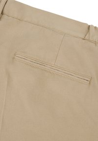 Poche arrière d'un pantalon beige avec une fente horizontale, détail de couture et taille partiellement élastiquée.