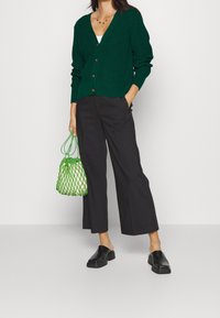 Grön ribbad cardigan med v-ringning och knappar, ihop med svarta vida byxor och en grön nätad väska. Svarta mules fulländar looken.