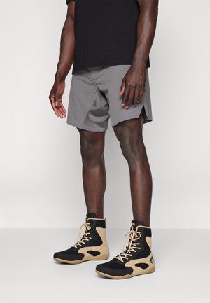 High-top athletic shoes in black mesh with tan suede accents and beige laces, paired with gray shorts featuring a split hem design.