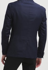 Granatowy blazer o dopasowanym kroju, gładkiej fakturze, z jednym rozcięciem z tyłu i guzikami przy mankietach. Wykonany z lekkiego materiału.