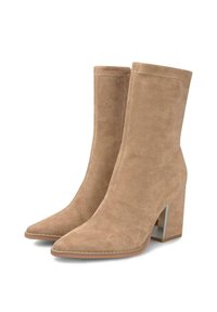 Un par de botas beige de gamuza hasta la pantorrilla con puntas afiladas y tacones gruesos en un fondo blanco.