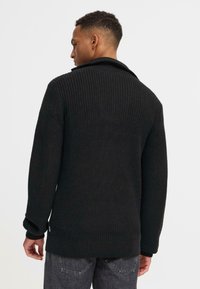 Schwarzer, gerippter Strickpullover mit hohem Kragen, strukturiertem Stoff, langen Ärmeln und lockerer Passform, mit einer Seitennähtedetail.
