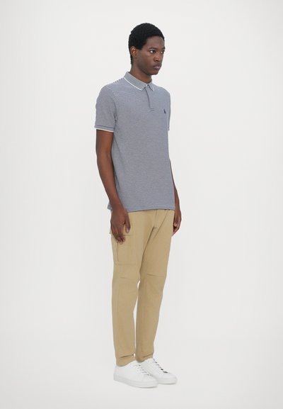 Polo con rayas azul marino y blancas, de manga corta y cuello tipo polo. Combinado con pantalones cargo color caqui y zapatillas blancas. Diseño minimalista.