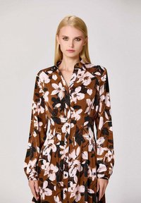 Robe marron à boutons avec un motif floral en rose et noir, dotée de manches longues et d'une taille ajustée, fabriquée à partir d'un tissu léger.